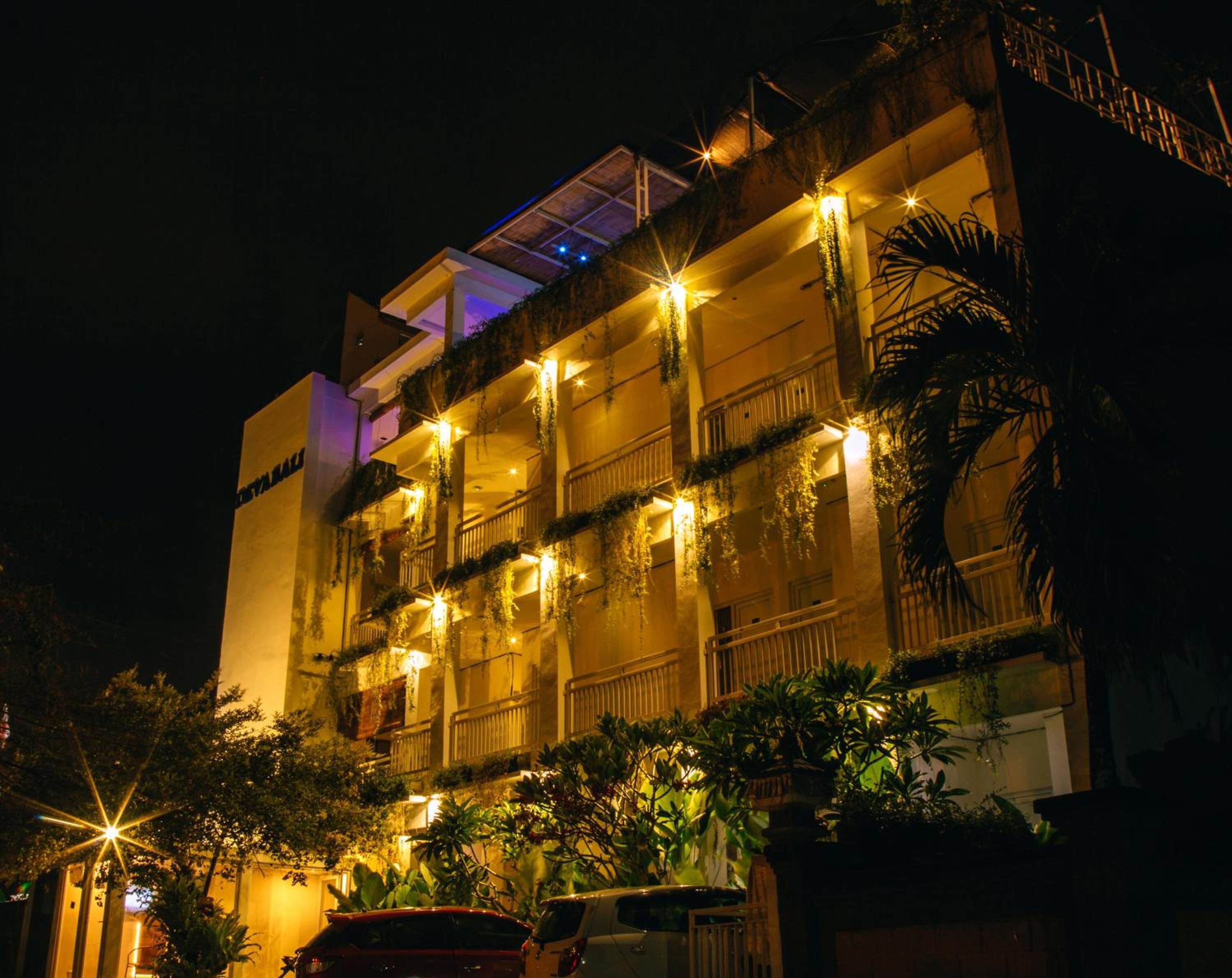 A multi-story hotel with balconies, outdoor lighting, and lush greenery.