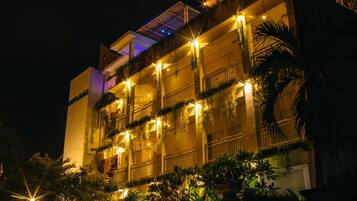 A multi-story hotel with balconies, outdoor lighting, and lush greenery.