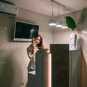 A modern interior with a flat-screen TV mounted on the wall, a podium with a person standing behind it, and a large potted plant on a shelf. - Deva Bali Apartment (Kerobokan)
