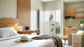 A hotel room with a bed, a desk, a chair, a TV, and a kitchenette.