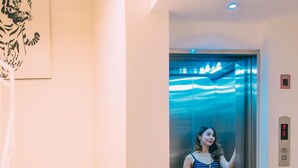 A woman standing in an elevator with a striped dress and a clutch, next to a staircase with beige steps. - Deva Bali Apartment (Kerobokan)