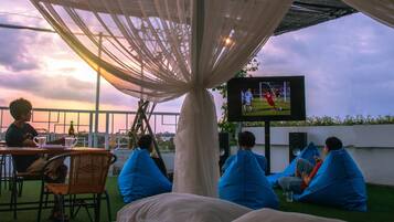 A group of people sitting on bean bags under a canopy, watching a soccer game on a TV screen.