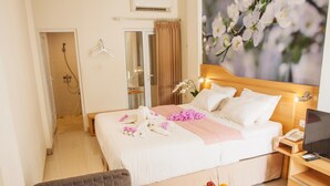 A hotel room with a bed, a TV, a bedside table with a phone, a shower area, and a fruit bowl on the floor. - Deva Bali Apartment (Kerobokan)