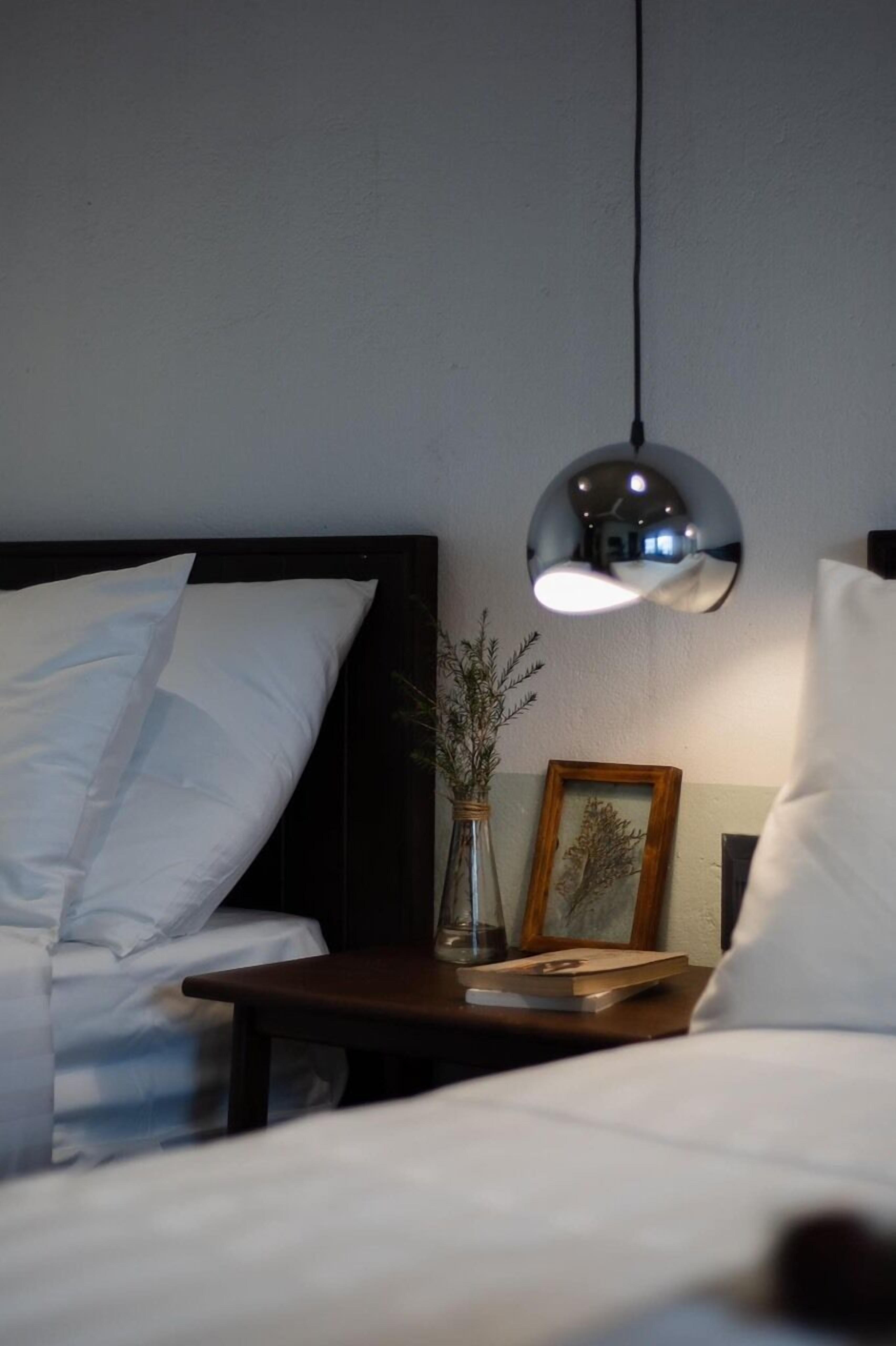 A neatly made bed with white linens, a bedside table with a vase of dried plants, and a framed picture.