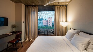 A hotel room with a large bed, a desk with a chair, a TV mounted on the wall, and a balcony with curtains. - The Note Dalat - Hostel (Xuan Huong - Da Lat)
