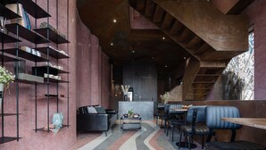 A modern interior with a curved wall, a seating area with a sofa and chairs, a coffee table, and a staircase. - The Note Dalat - Hostel (Xuan Huong - Da Lat)