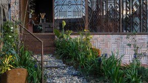A building entrance with a brick facade, a geometric patterned gate, and a gravel pathway with plants. - The Note Dalat - Hostel (Xuan Huong - Da Lat)