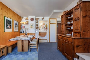 Una habitación acogedora con un banco de madera, una mesa de comedor con mantel a cuadros y un armario grande de madera.