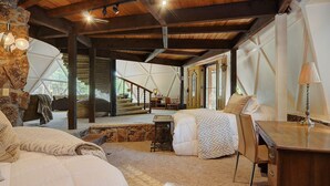 A spacious bedroom with a large bed, a desk, and a chair. There is a staircase leading to an upper level. - PRIVATE INDOOR HOT SPRINGS POOL~RETRO GEODESIC DOME~CHALK CLIFFS VIEW~WILDLIFE (Nathrop)