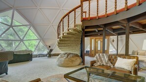 A spacious living area with a large window, a spiral staircase, and a cozy seating arrangement. - PRIVATE INDOOR HOT SPRINGS POOL~RETRO GEODESIC DOME~CHALK CLIFFS VIEW~WILDLIFE (Nathrop)