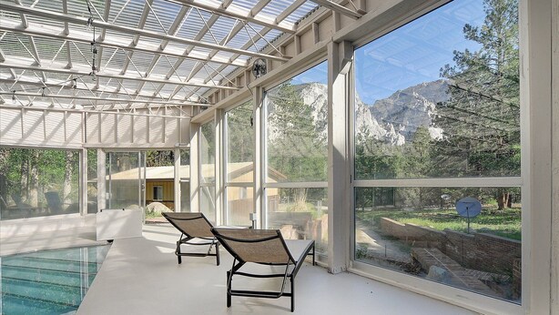 A sunlit indoor swimming pool area with two lounge chairs, large windows offering mountain views, and a glass ceiling structure. - PRIVATE INDOOR HOT SPRINGS POOL~RETRO GEODESIC DOME~CHALK CLIFFS VIEW~WILDLIFE (Nathrop)