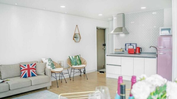 A modern living room with a sofa, two chairs, and a small table. There is a kitchen area with a stove, sink, and refrigerator. - Blooming Pension (Geoje)