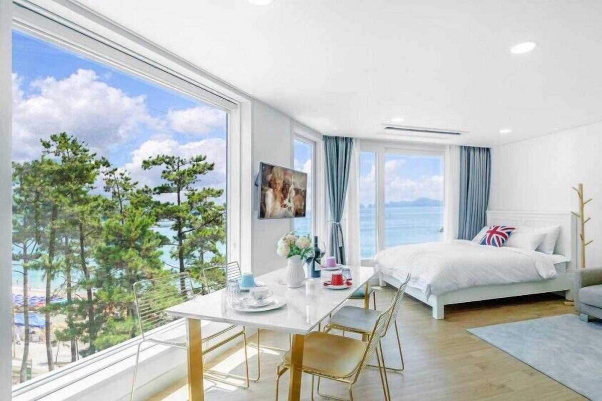 A modern hotel room with a large window offering a scenic view of trees and the sea.