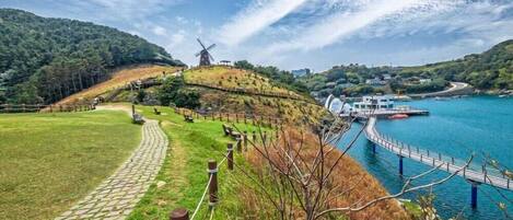 A scenic landscape with a windmill, a stone pathway, and a body of water with a bridge.