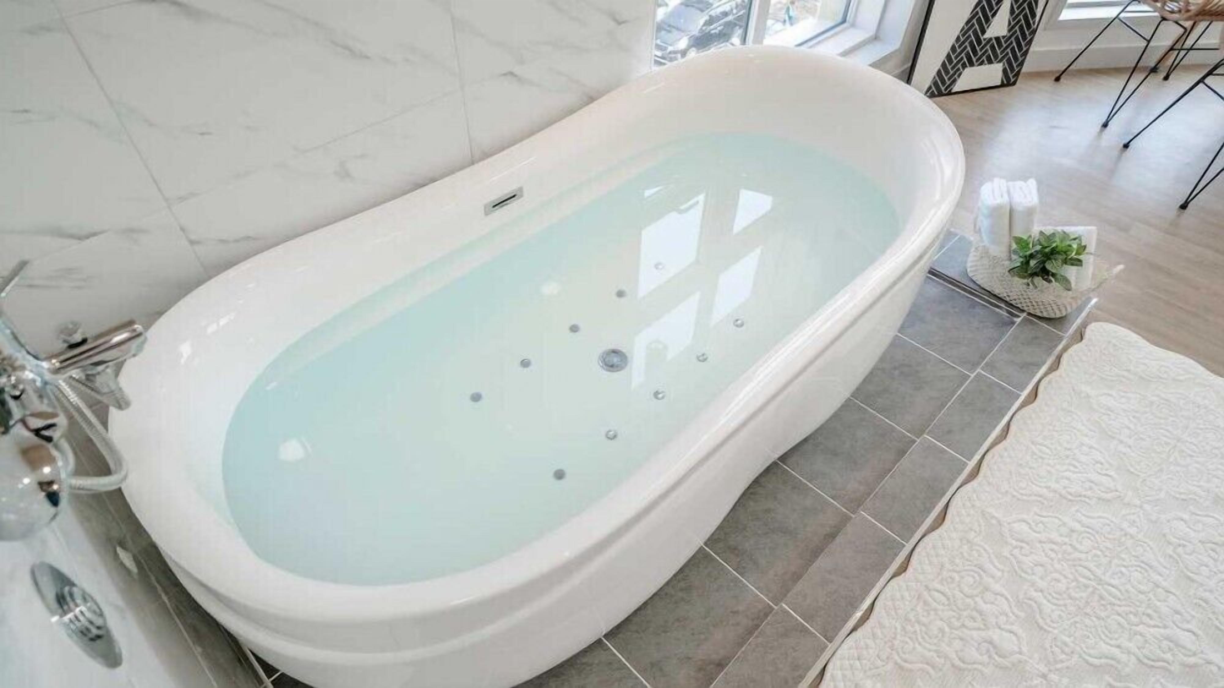 A modern bathroom with a freestanding bathtub, grey tiled floor, and a white textured rug.