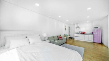 Una habitación de hotel moderna con una cama grande, un sofá, una mesita y una kitchenette.