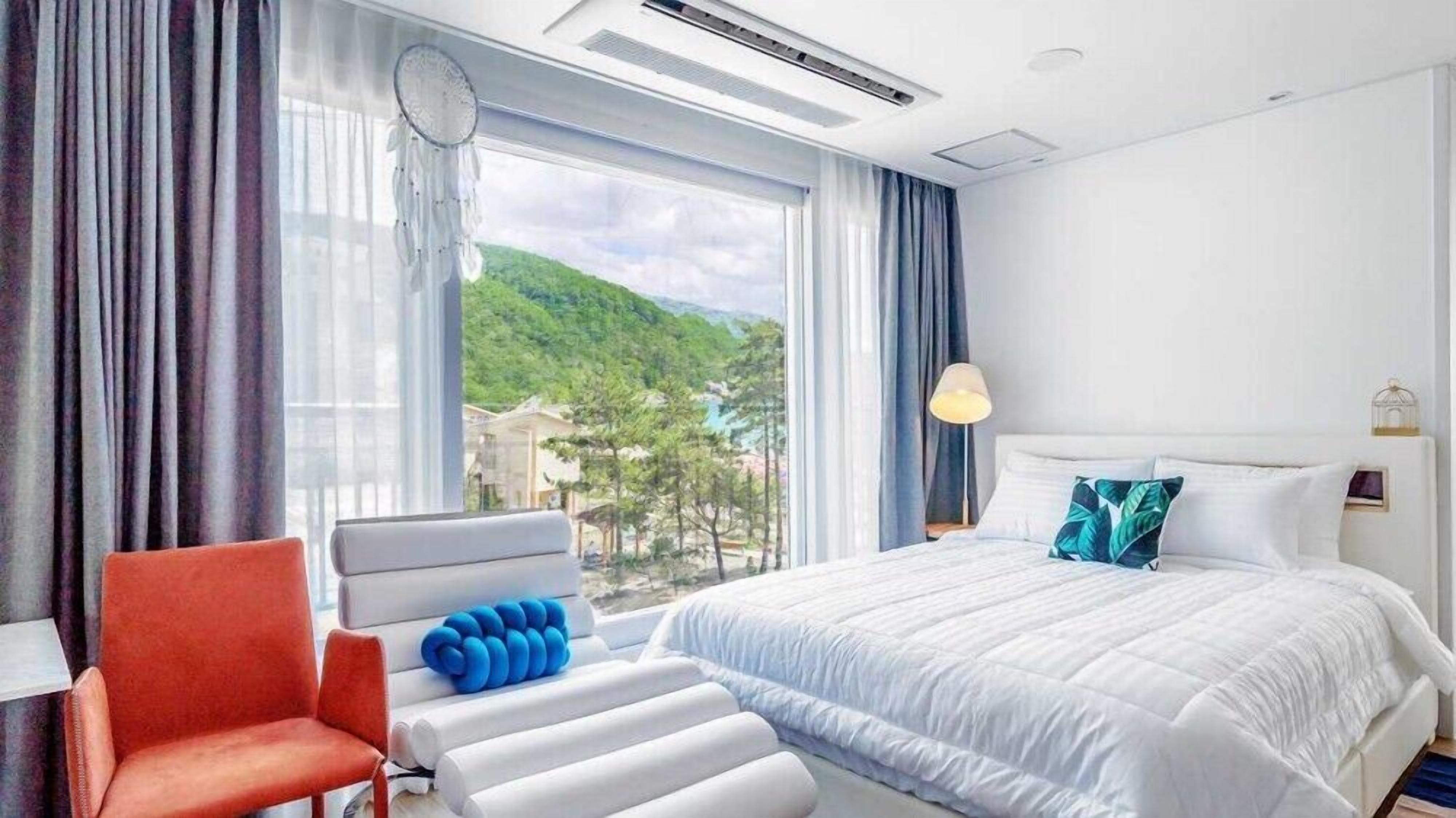 Una habitación de hotel con cama, una silla, una lámpara y vista a la montaña.