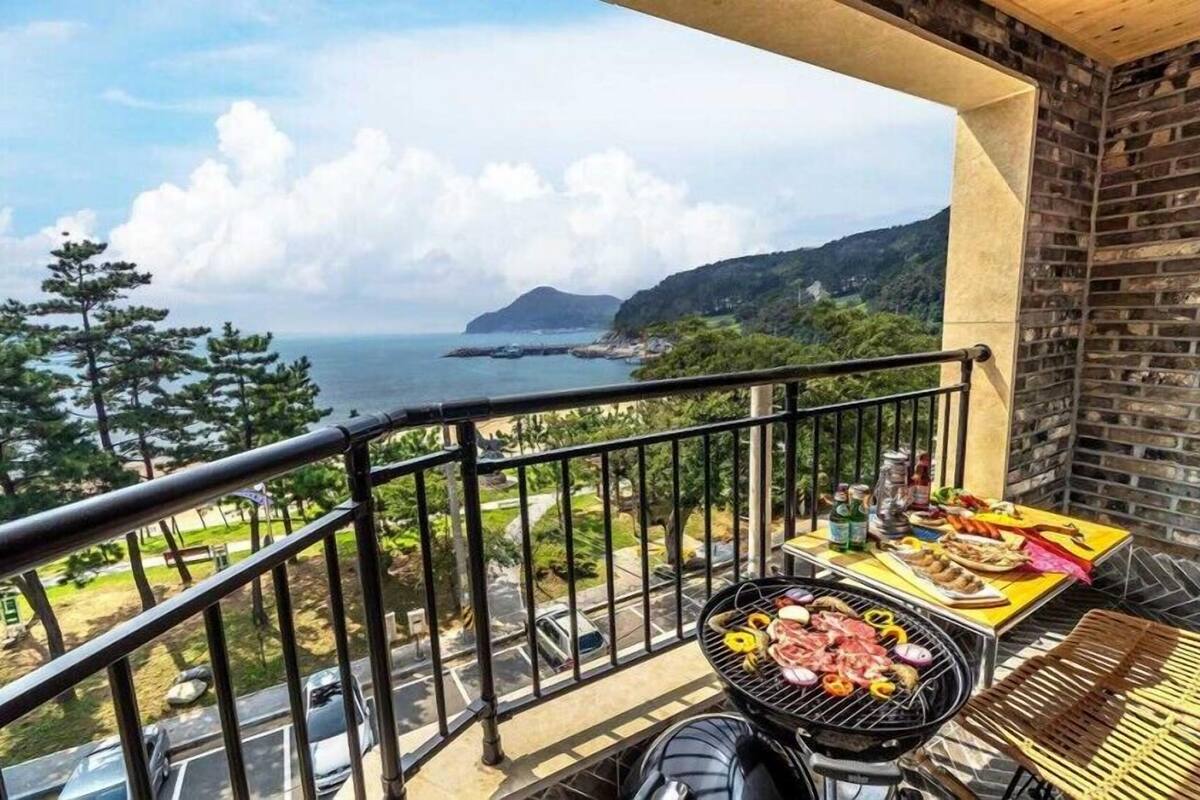 A balcony with a grill, a table with food, and a view of the sea and mountains.