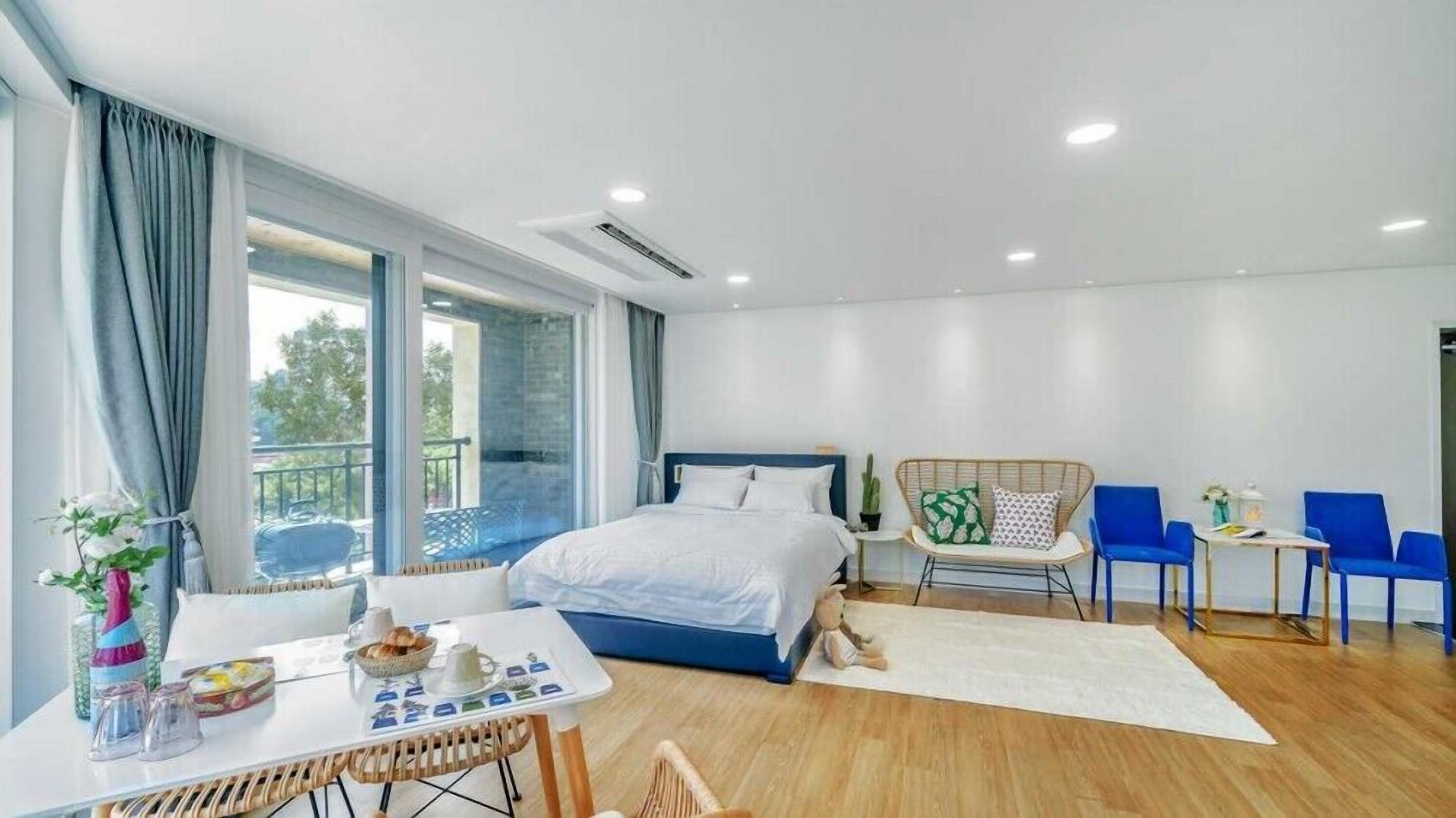 Una habitación de hotel moderna con una cama grande, una mesa de comedor con alimentos para el desayuno, un sofá y un balcón con vistas.