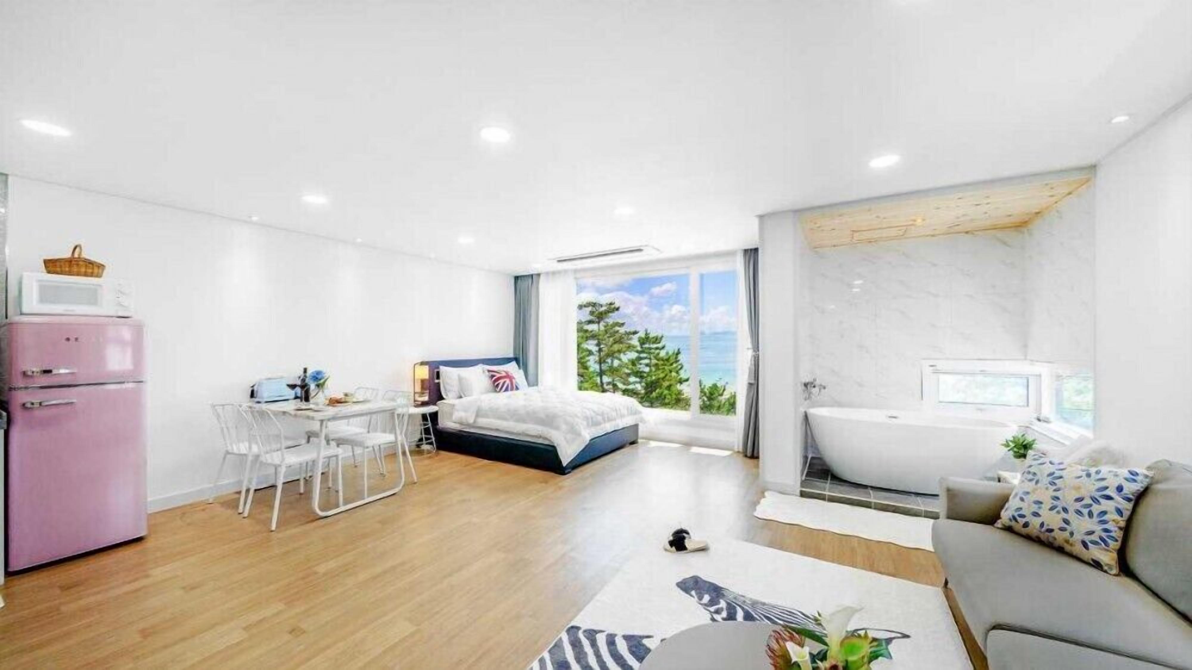 Un dormitorio moderno con cama, escritorio, refrigerador rosa y vista al exterior.
