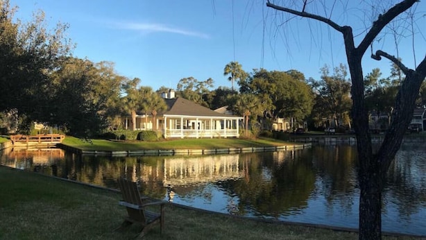 Een huis met een vijver, een houten steiger en een stoel aan het water.
