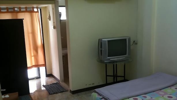 A bedroom with a bed, a television on a stand, and a door leading to another room. - Suayai Guesthouse (Bangkok)