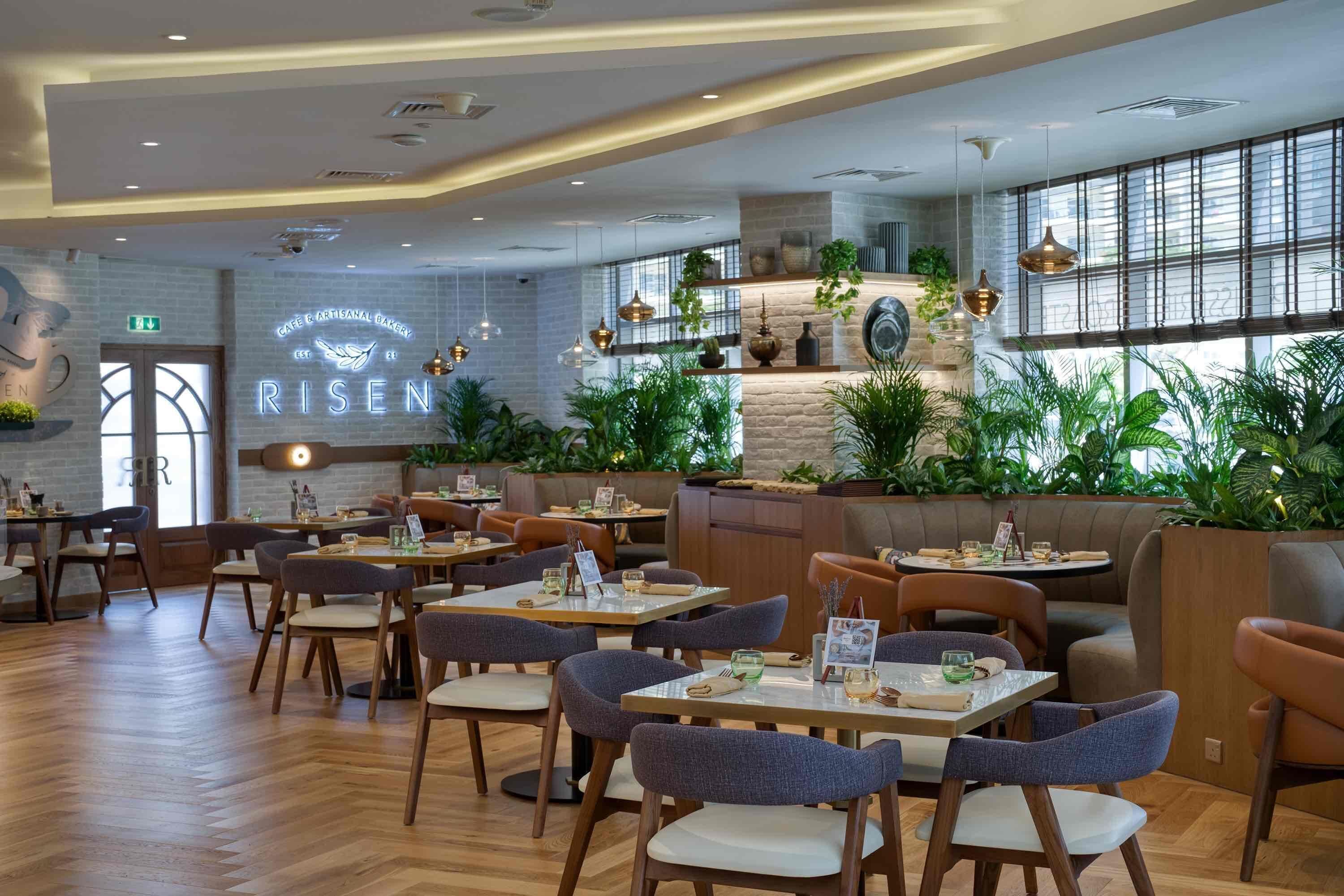 A modern cafe interior with wooden tables, cushioned chairs, and a large illuminated sign.