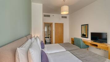 A hotel room with a bed, a desk with a TV, and a bathroom visible through an open door.