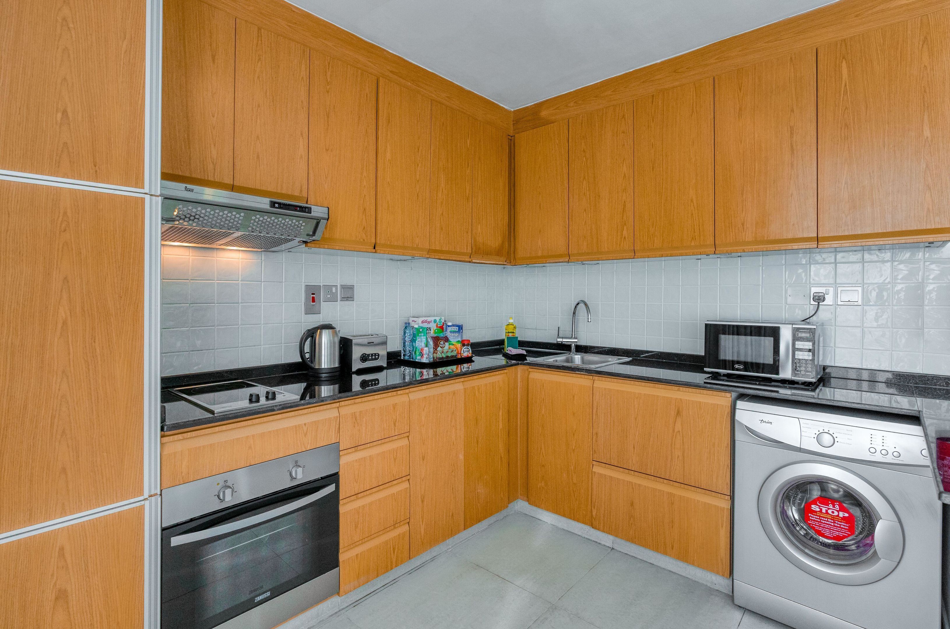A kitchen with wooden cabinets, a microwave, a washing machine, and a toaster.