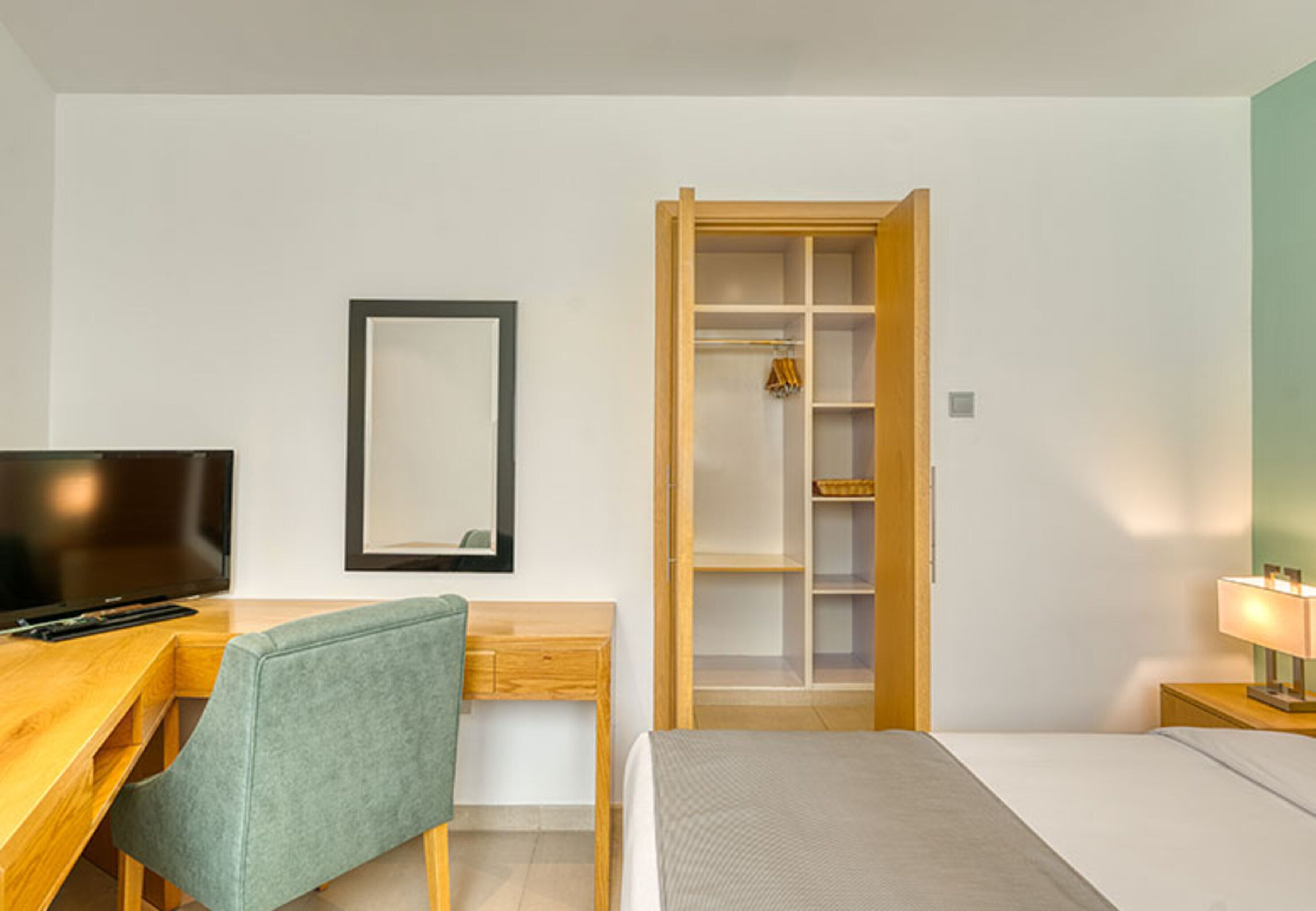 Une chambre d’hôtel comprenant un lit, un bureau avec une chaise, une télévision, une armoire et une table de chevet avec une lampe.