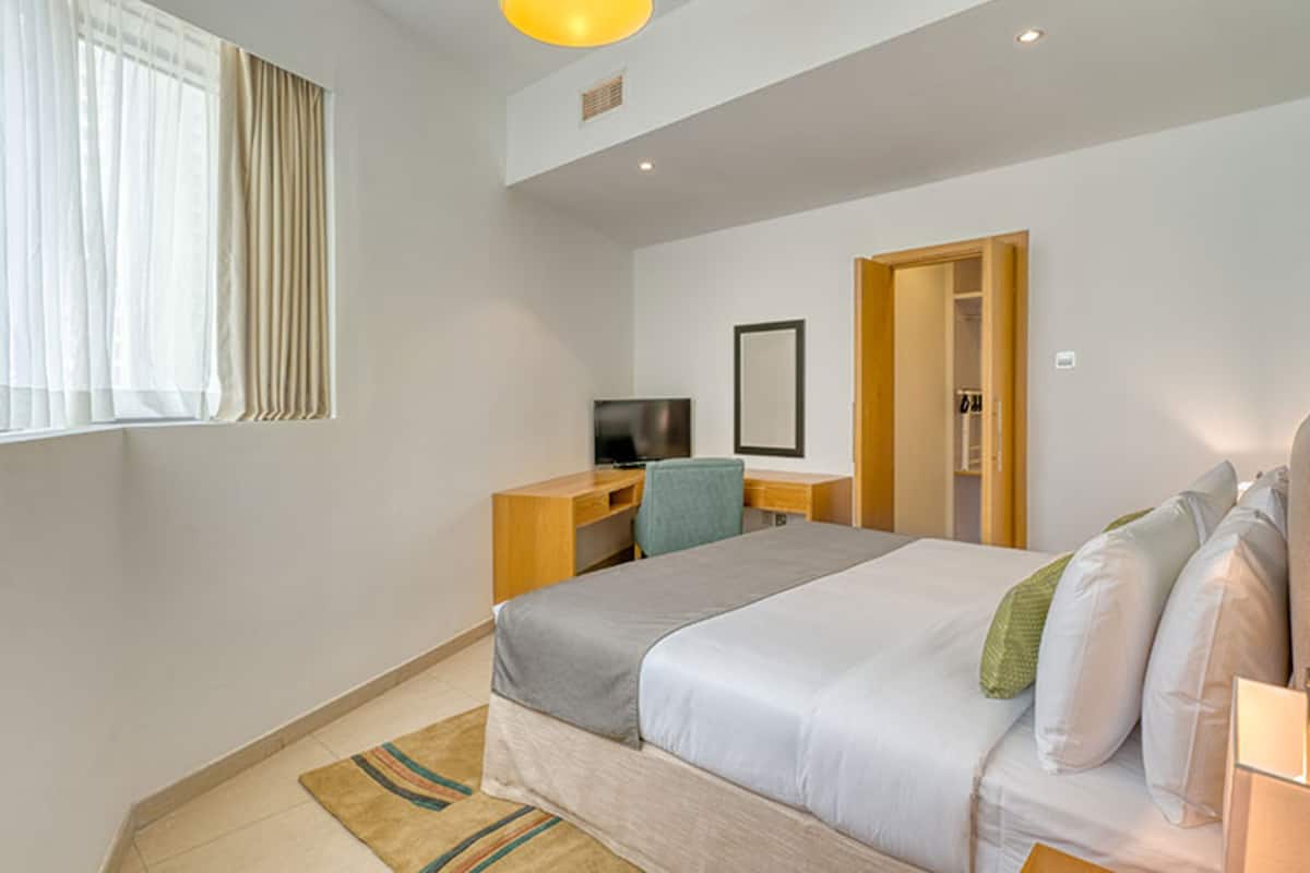 Une chambre d’hôtel comprenant un lit, un bureau, une télévision et une porte donnant sur une salle de bain.