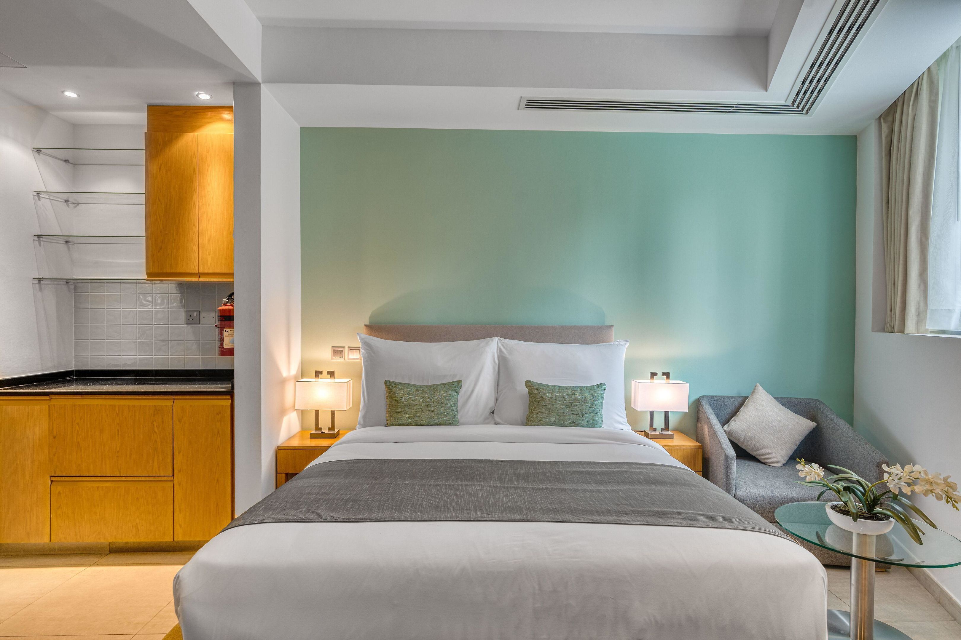 Een hotelkamer met een bed, een bank, een kleintje tafeltje met een plant, een kitchenette en een badkamer.