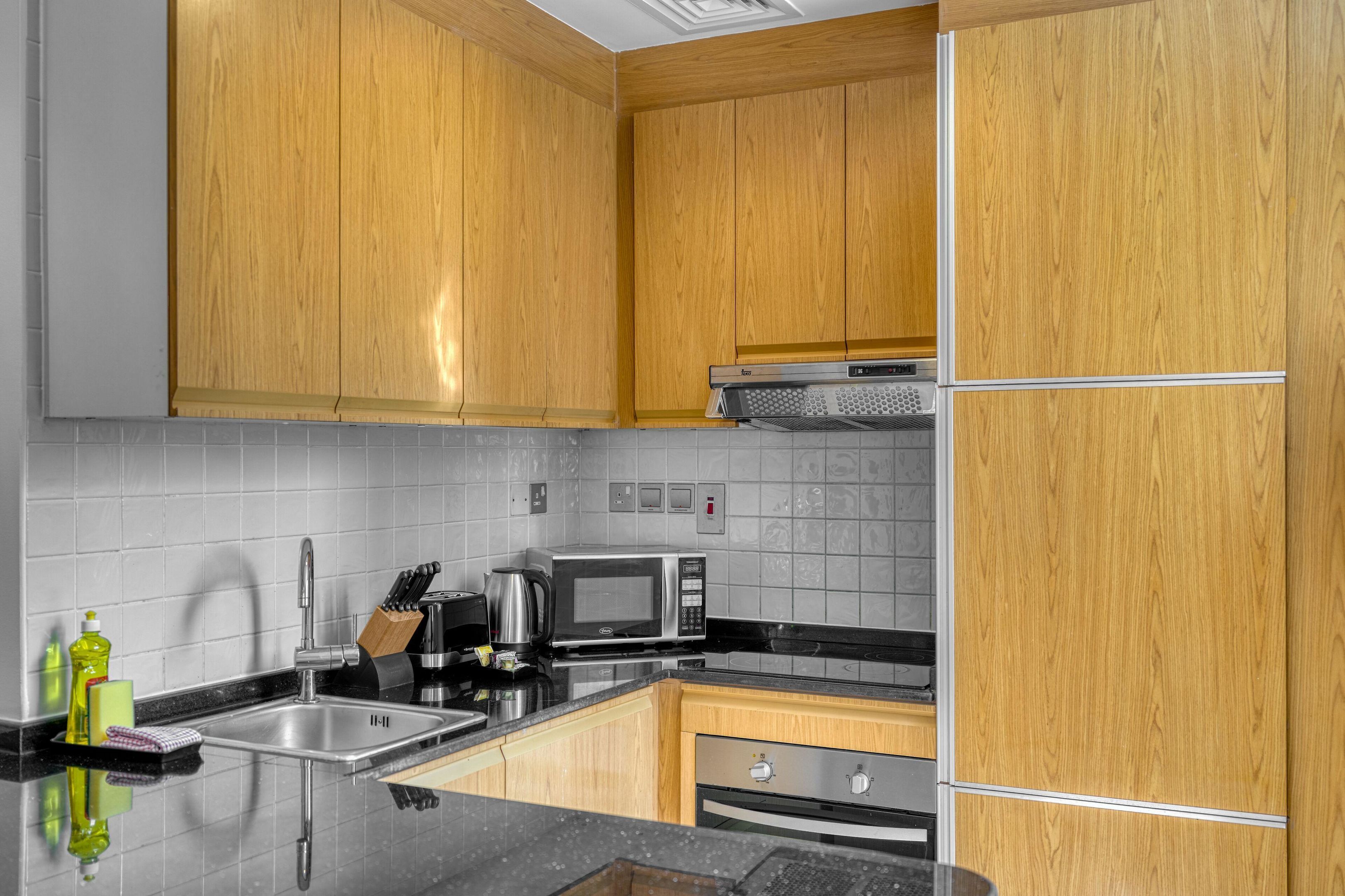Una cocina con armarios de madera, un lavamanos de acero inoxidable, un microondas y un horno empotrado.