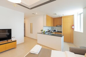 Une chambre d’hôtel moderne équipée d’un téléviseur à écran plat, d’un meuble TV en bois, d’un lit, d’un petit canapé, d’une kitchenette avec un four à micro-ondes et d’une fenêtre.