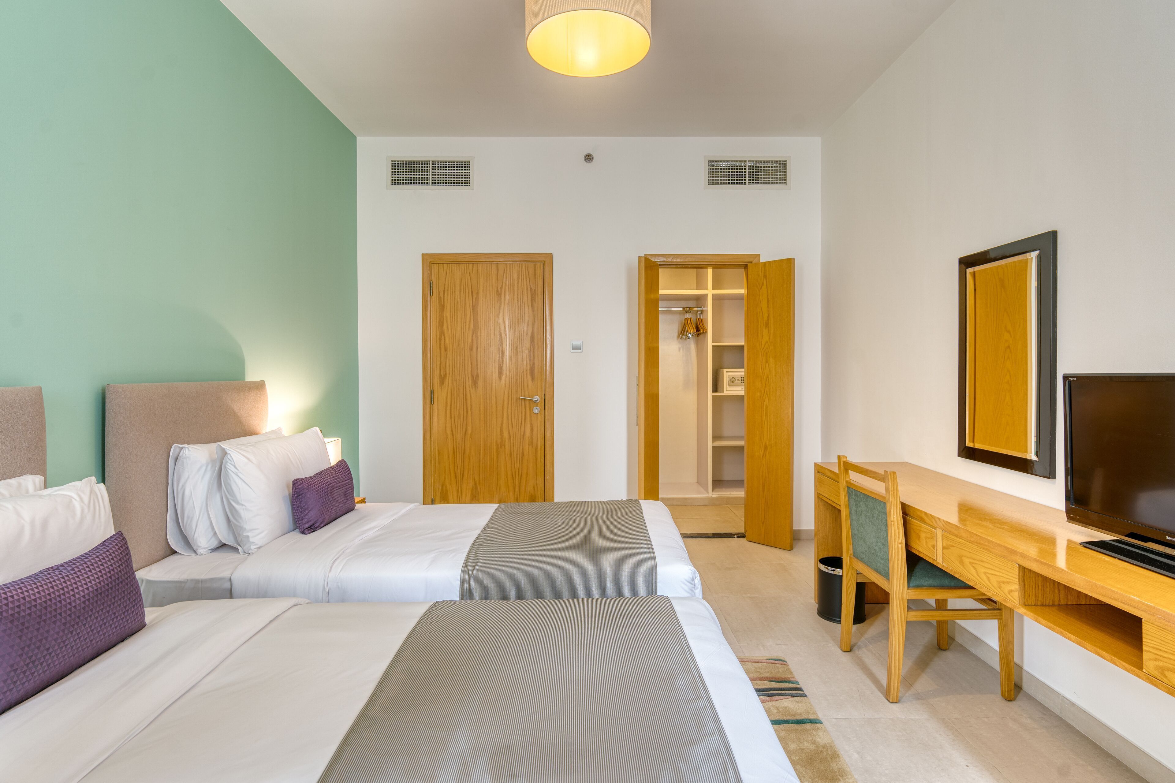 Una habitación de hotel con dos camas, un escritorio, un televisor y un armario.