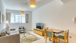 Een moderne woonkamer met een bank, een eettafel met stoelen, een televisie en een groot raam met gordijnen.