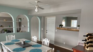 A dining area with a white table, blue placemats, white chairs, a ceiling fan, and a wooden wine rack. - Lake view with pool (Okanagan Falls)
