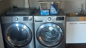 A laundry area with two front-loading washing machines, a basket, and a bottle of laundry detergent. - Lake view with pool (Okanagan Falls)