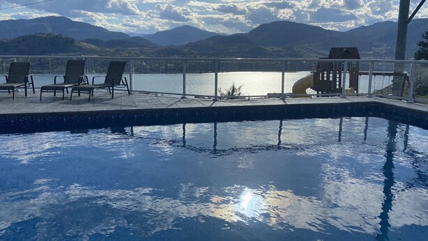 A swimming pool with lounge chairs and a view of mountains and a lake. - Lake view with pool (Okanagan Falls)