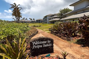 Explore the beautifully landscaped grounds of Poipu Sands, featuring a well-maintained pathway and lush tropical vegetation.