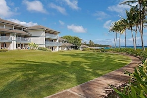 Een hotel met een groot gazon, een betonnen pad en uitzicht op de oceaan.