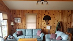 A cozy living room with wooden paneling, two light blue sofas with cushions, a wooden coffee table, and a lamp.