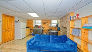 Un espacio habitable pequeño con kitchenette, un sofá azul, estanterías de madera y una pared de ladrillo.