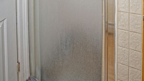 Un baño con mampara de ducha de vidrio esmerilado, una puerta blanca y paredes de azulejos.