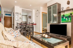 A living room with a sofa, TV, and a dining area with chairs and a table.