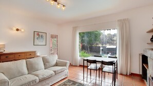 A living room with a sofa, dining table, chairs, a fireplace, and a large window with curtains. - Villa "La Alpispa" in the countryside with Pool, Wi-Fi, Terrace & Garden (Los Hoyos)
