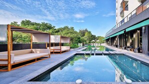 Uma área moderna de piscina ao ar livre com espreguiçadeiras e um edifício com paredes de vidro.