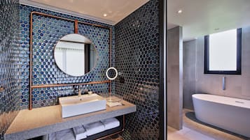 A modern bathroom with a hexagonal mosaic tile wall, a round mirror, a sink with a towel rack, and a standalone bathtub.