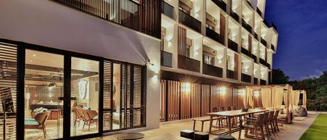 A modern hotel with a spacious outdoor dining area, multiple balconies, and a well-lit entrance.