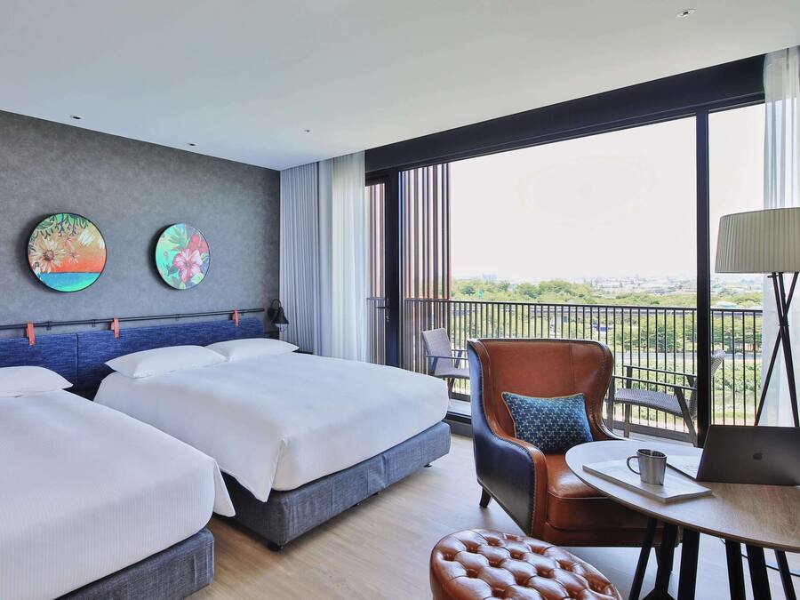Habitación de hotel con dos camas, un sofá, una silla, una mesa, una computadora portátil y un balcón con vistas.